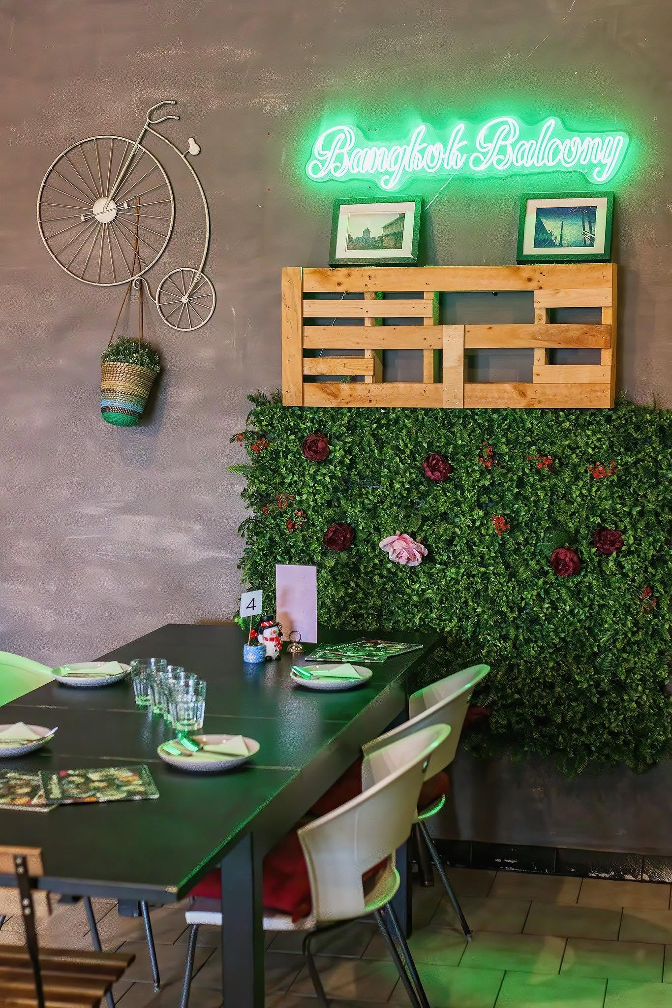 Green neon Bangkok Balcony sign above a leafy wall and a set dining table